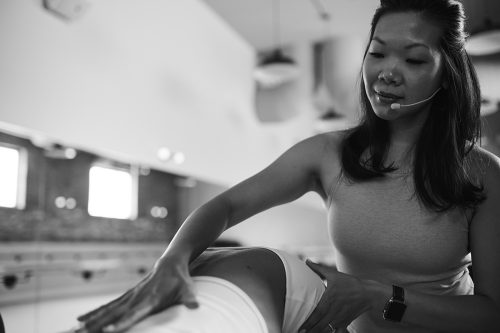 A barre instructor is wearing a headset while adjusting a student’s form.