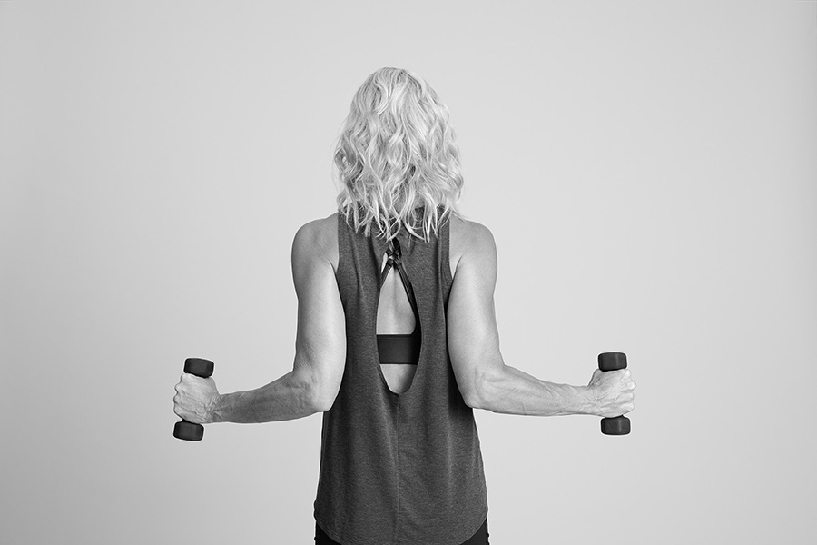 Woman in a barre studio demonstrating a lat pull exercise with dumbbells.