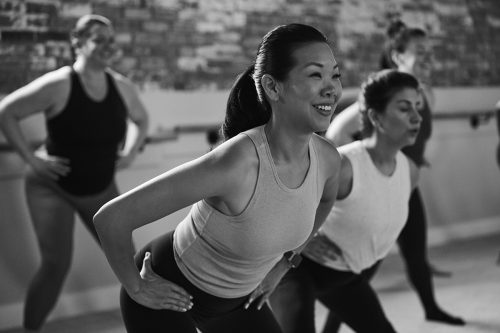 Four people with their hands on their hips doing a lower-body strengthening move during a barre class.