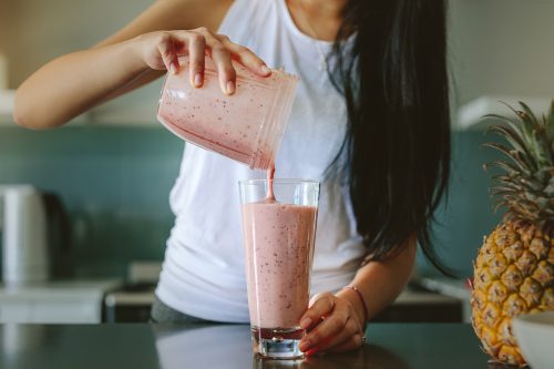 Woman pouring a pink smoothie made with berries and protein powder, a refreshing recovery drink to refuel muscles after exercise.