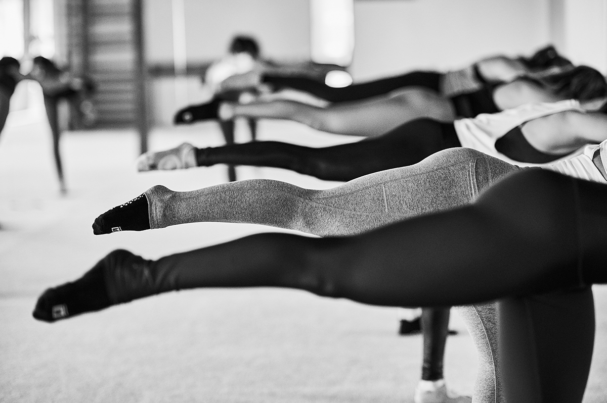 Bar Method students are reaching for the barre while pointing their right leg back.