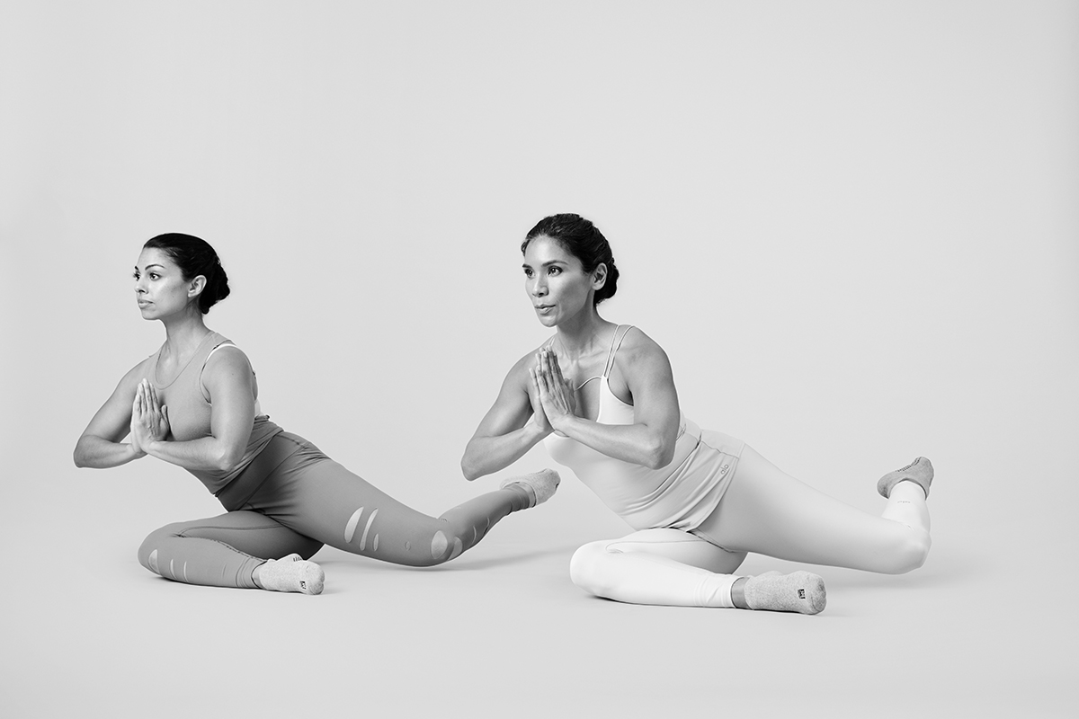 Two women in barre workout gear doing a seated pretzel exercise to create more toned glutes.