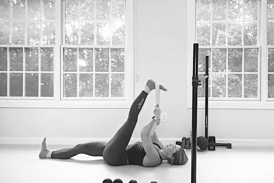 Woman in a barre studio doing a strap stretch after a workout for toned glutes.