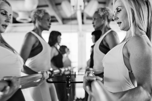 Group of individuals engaged in barre exercises, using the mirror for form correction, optimal performance, and alignment in a fitness studio.