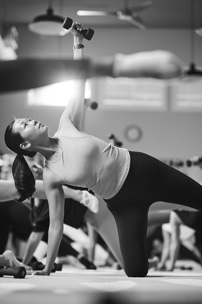 Woman in a Bar Method studio performing an upper-body exercise with a dumbbell.