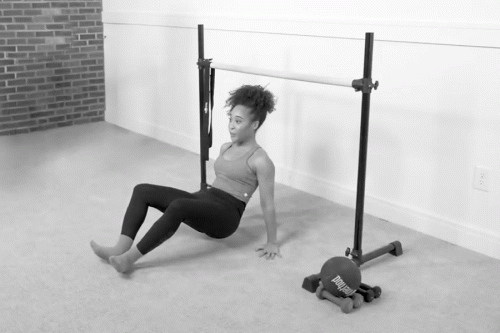 Woman in a Bar Method studio performing a reverse push-up on the floor near the ballet barre.