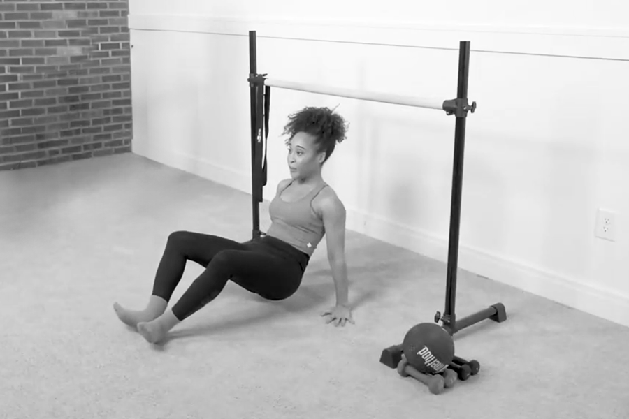 Woman in a Bar Method studio performing a reverse push-up on the floor near the ballet barre.