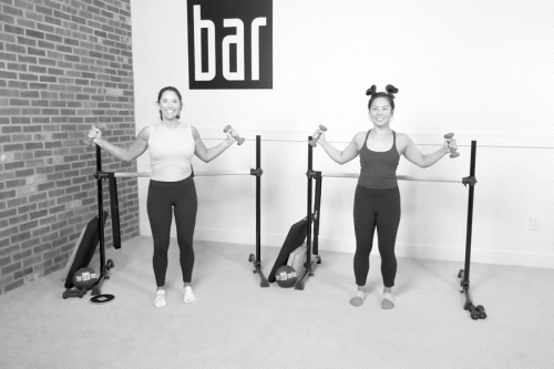 Two women in a Bar Method studio demonstrating rhomboid pulls with light dumbbells.