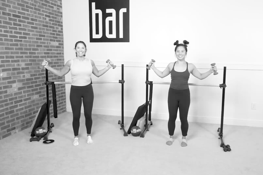 Two women in a Bar Method studio demonstrating rhomboid pulls with light dumbbells.