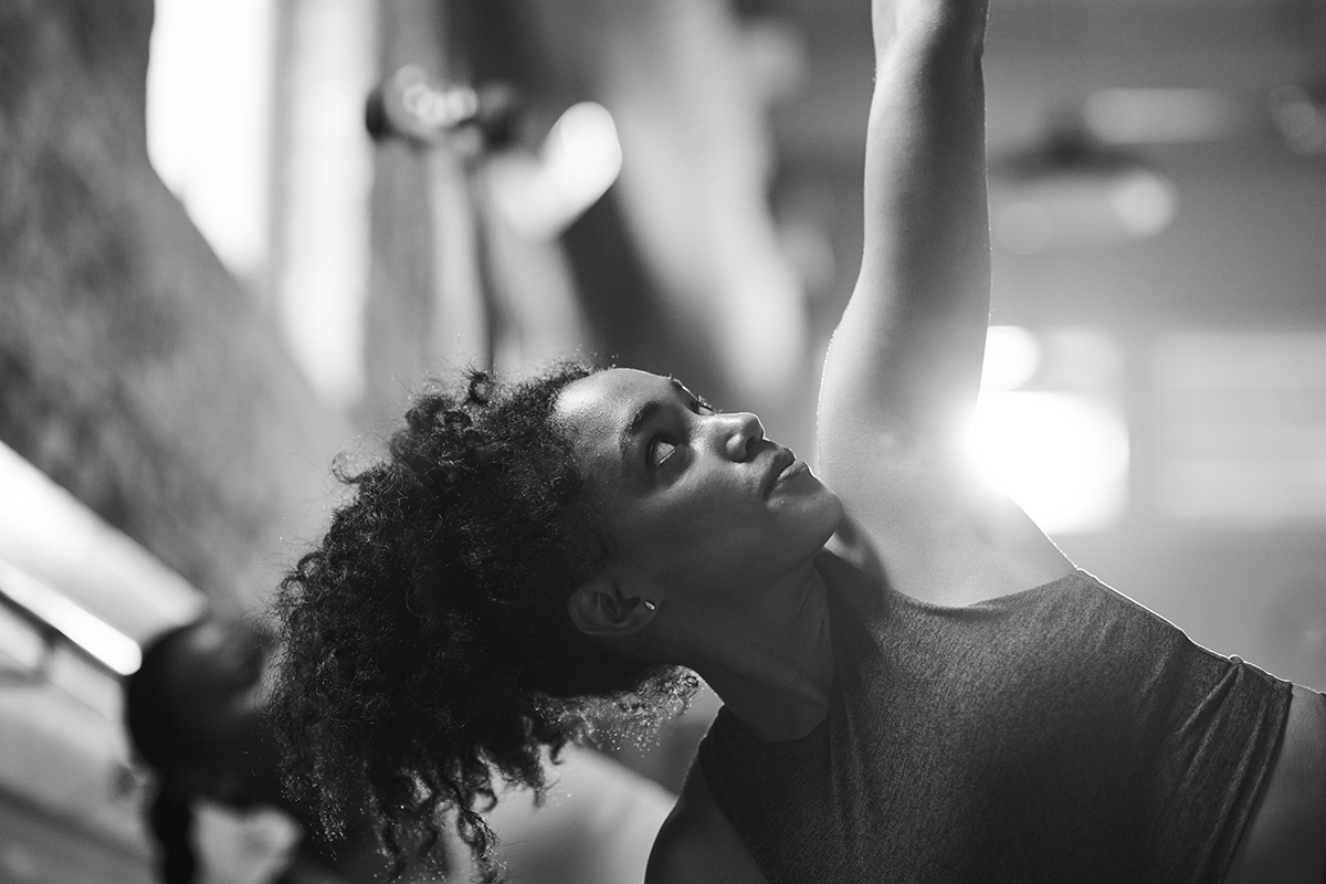 Woman in a Bar Method studio stretching her arm upward to prepare for an upper-body barre workout.