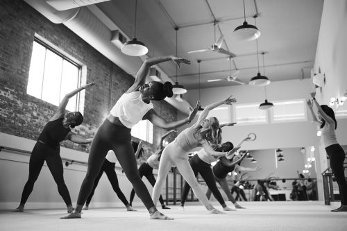 A group of women performing synchronized side stretches in a bright studio, highlighting the blend of strength and grace in barre fitness.