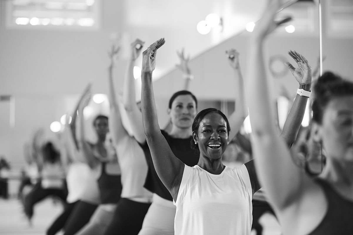 Black and white image of woman smiling and resting her head on the Barre after completing a workout