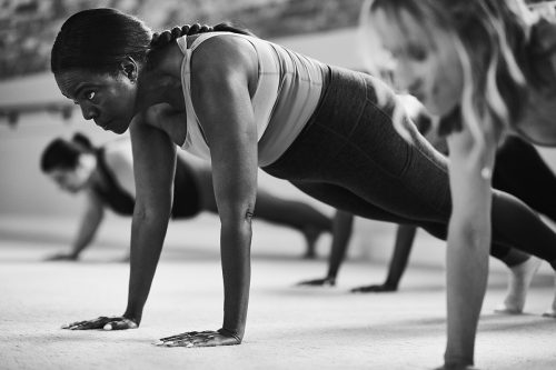 Group of women performing isometric exercises on the floor in a barre studio.