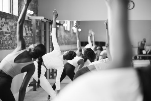 Group of women performing a stretch and extending their arms upward in a barre studio.