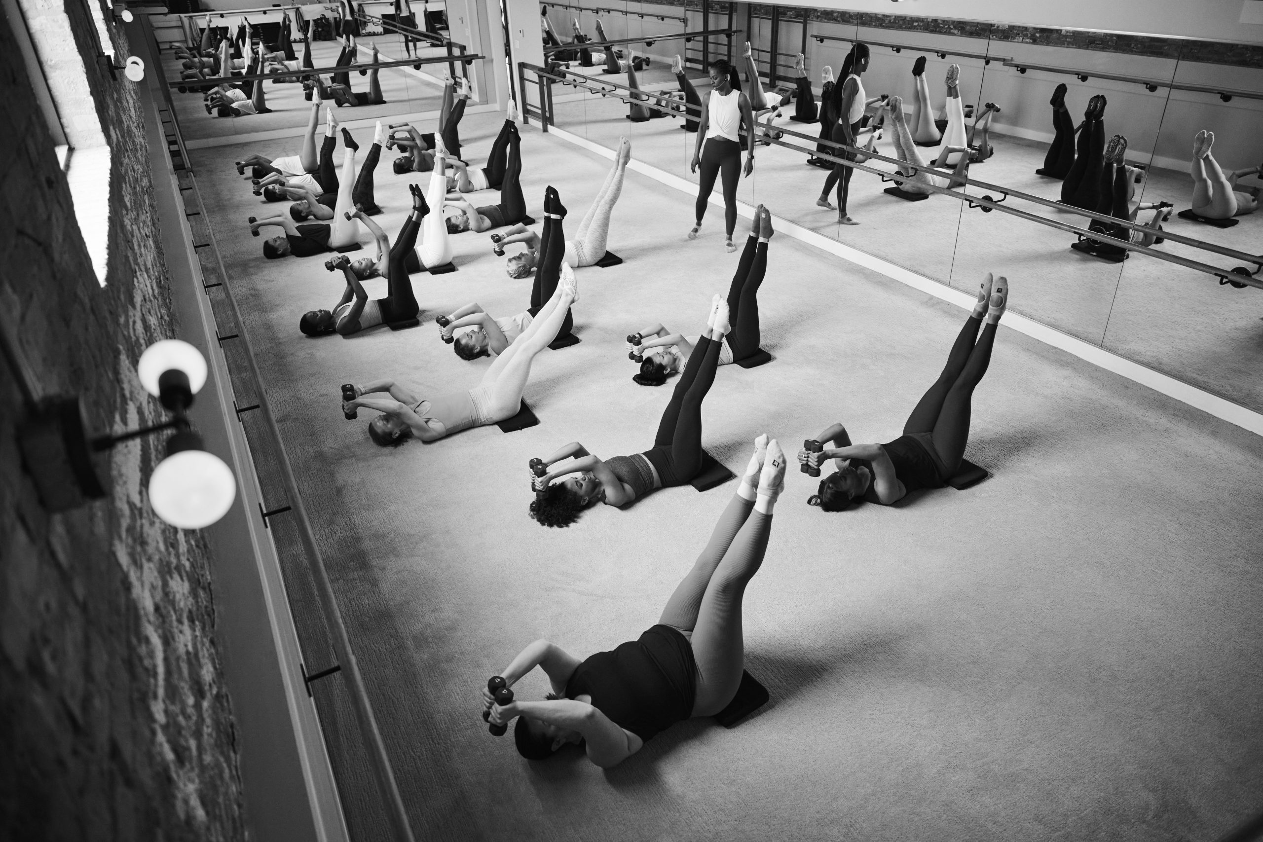Black and white image of woman smiling and resting her head on the Barre after completing a workout