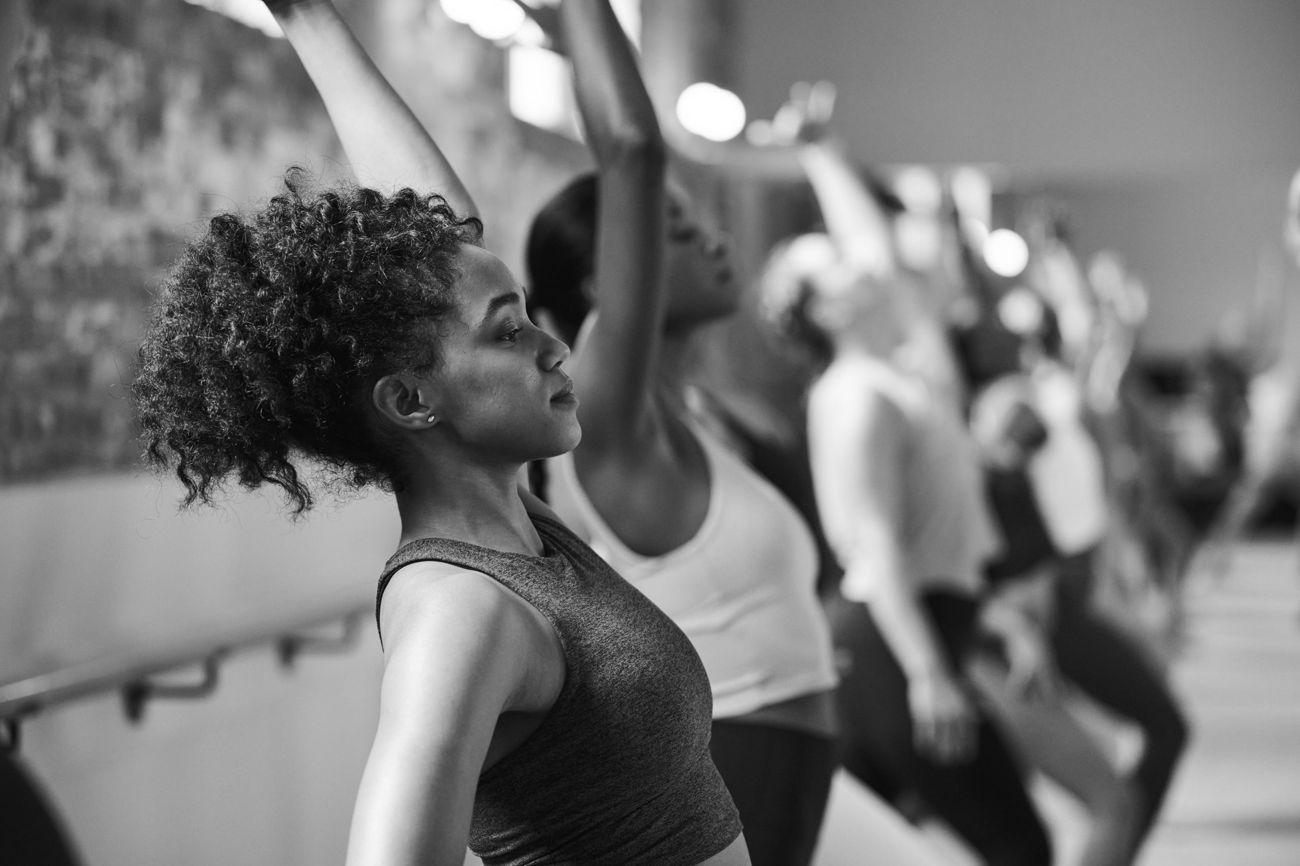 Black and white image of woman smiling and resting her head on the Barre after completing a workout