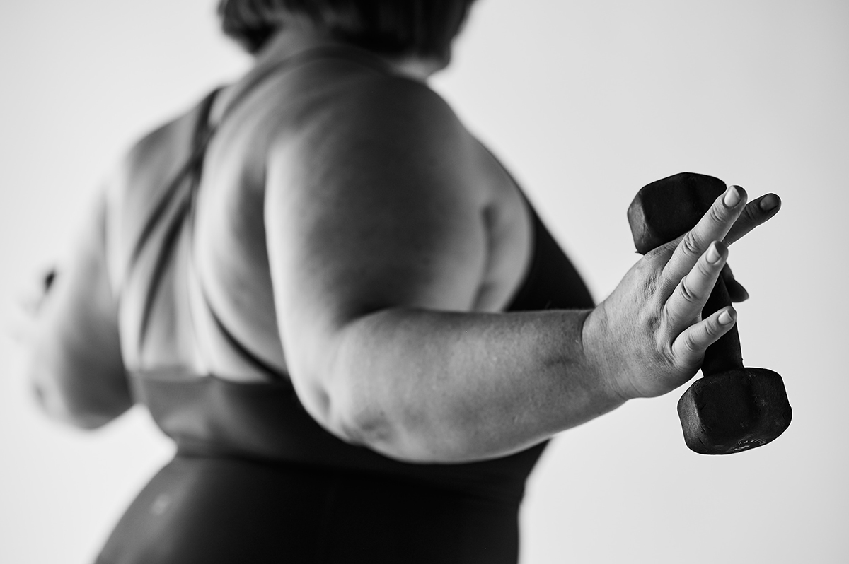 Woman in athletic gear doing a back exercise with a light dumbbell.