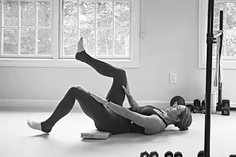 Woman in a barre studio demonstrating flatback curl tabletop, one of the stability exercises featured in The Bar Method.