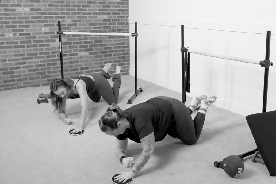 Bar Method instructor teaching a member how to do forearm planks with a slider, one of the stability exercises found in The Bar Method.