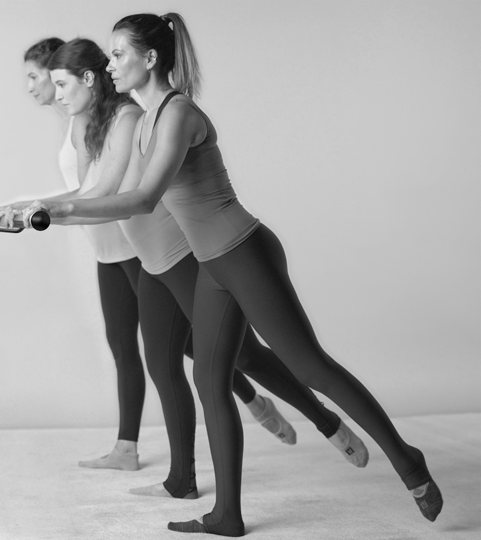 Three women standing at a ballet barre performing diagonal seat, part of a prenatal core workout.